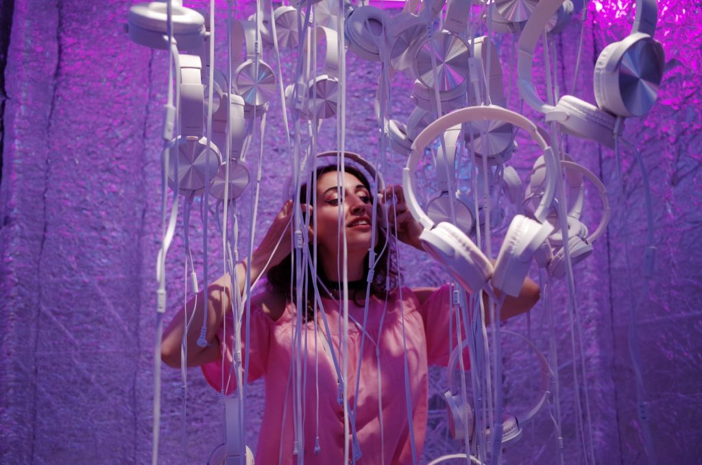 photo of woman wearing pink shirt standing near white headphones against purple background